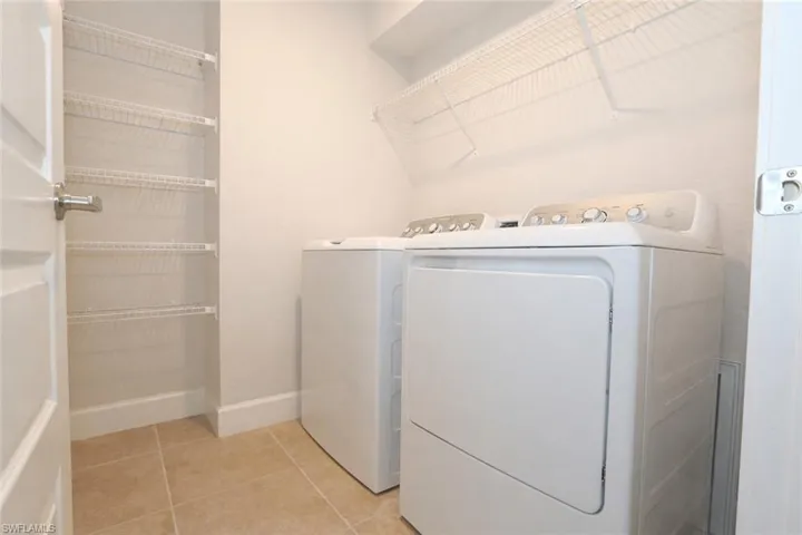This utility area features white walls, tiled flooring, a washer and dryer, and wire shelving for storage