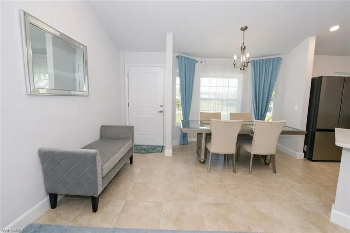 The property features tiled flooring throughout the open living spaces, a dining area with a chandelier and large windows, and a kitchen area with a refrigerator