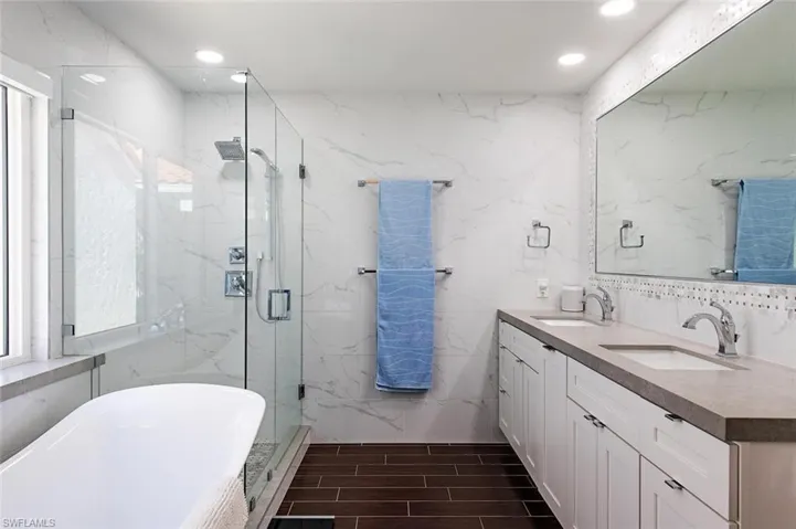 Full bath featuring tile walls, a soaking tub, double vanity, a marble finish shower, and wood tiled floors
