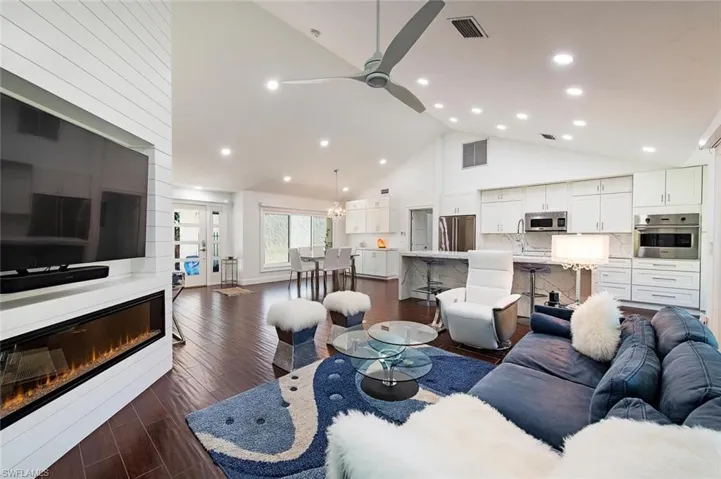 Living area with high vaulted ceiling, dark wood finished floors, a glass covered fireplace, a ceiling fan, and recessed lighting