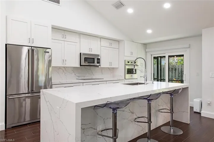 Kitchen featuring wood tiled floors, appliances with stainless steel finishes, light stone counters, recessed lighting, and white cabinetry