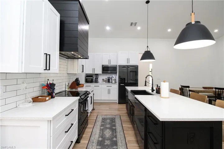 Kitchen featuring an island with sink, black appliances, white cabinetry, and hanging light fixtures