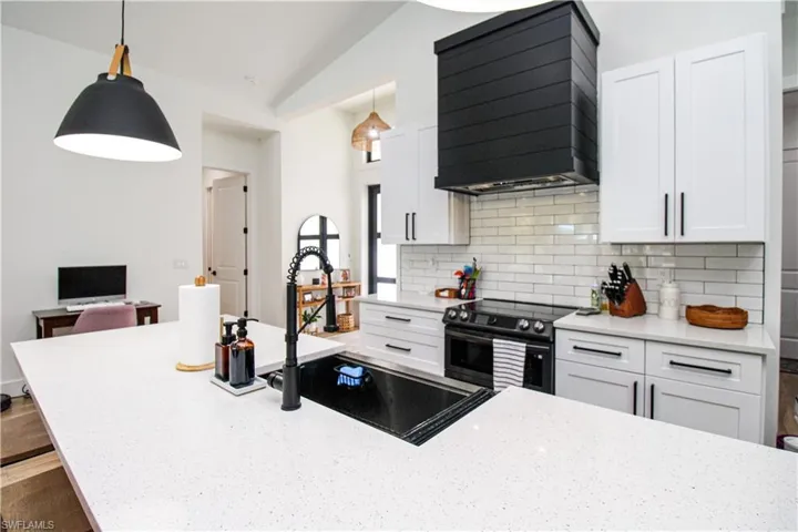 Kitchen featuring white cabinets, custom exhaust hood, stainless steel electric range, decorative light fixtures, and vaulted ceiling