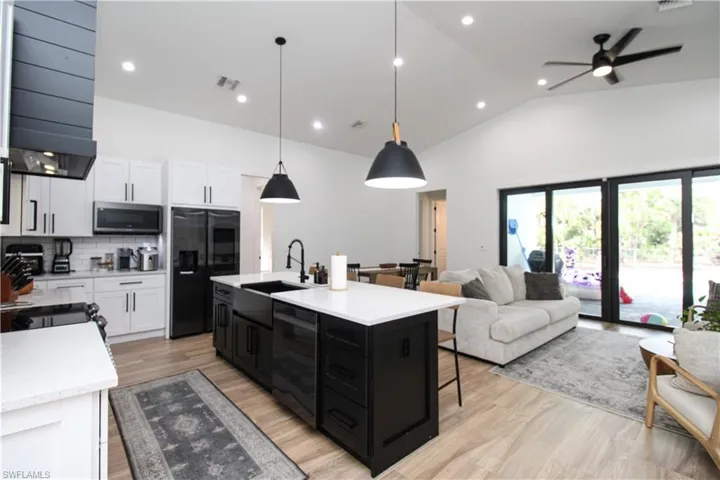 Kitchen featuring white cabinets, wine cooler, hanging light fixtures, a kitchen island with sink, and black refrigerator with ice dispenser