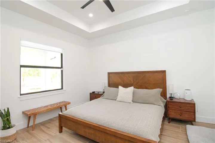 Bedroom featuring ceiling fan, light hardwood / wood-style flooring, and a tray ceiling