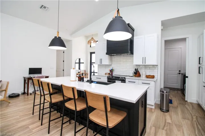 Kitchen featuring white cabinetry, an island with sink, pendant lighting, lofted ceiling, and sink