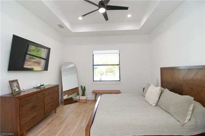 Bedroom featuring light hardwood / wood-style flooring, ceiling fan, and a raised ceiling