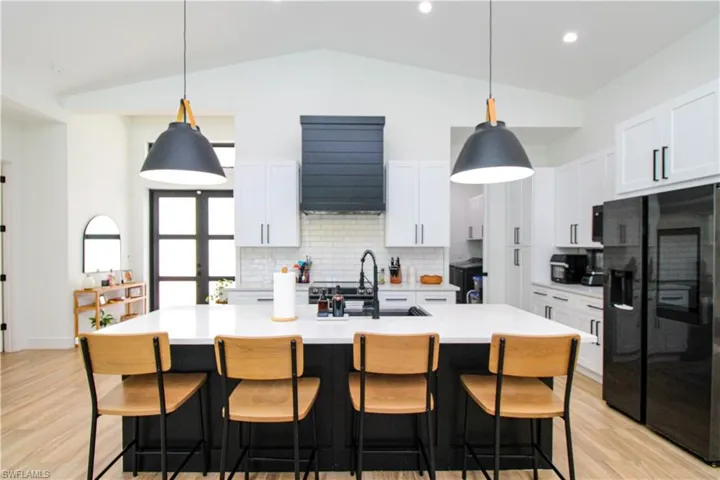 Kitchen featuring black fridge, a center island with sink, lofted ceiling, and white cabinetry