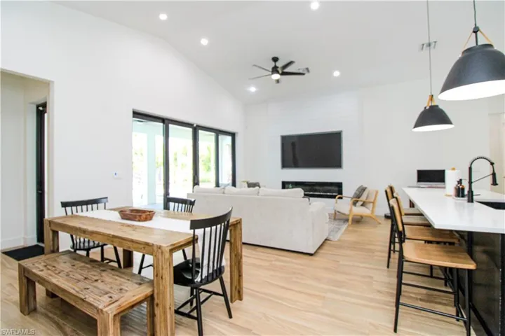 Dining area with ceiling fan, sink, light hardwood / wood-style flooring, high vaulted ceiling, and a large fireplace