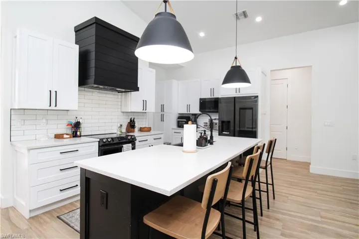 Kitchen featuring pendant lighting, a kitchen island with sink, custom range hood, range with electric cooktop, and refrigerator with ice dispenser