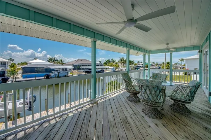 Covered outdoor deck featuring weathered wood flooring, two ceiling fans, and a white railing