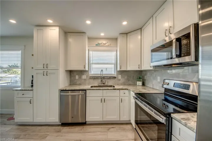 Modern kitchen featuring white shaker cabinetry, stainless steel appliances, speckled stone countertops, and a gray tile backsplash