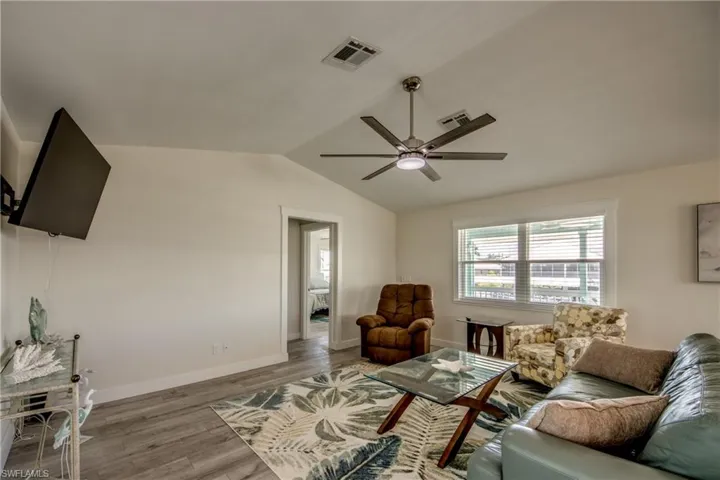Vaulted ceiling living area featuring wood-finish flooring, a contemporary ceiling fan, and a wall-mounted television