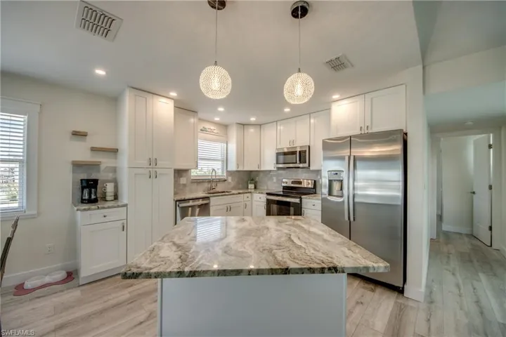 Kitchen featuring a central island with a stone countertop, white shaker cabinetry, stainless steel appliances, and recessed lighting