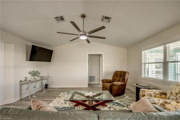 Spacious living area featuring a vaulted ceiling with a modern ceiling fan, wood-finish flooring, and a large window with blinds