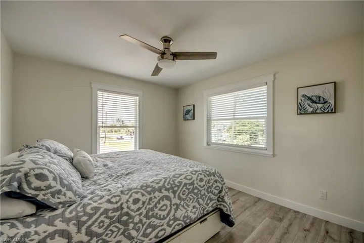 Spacious room featuring light wood-finish flooring, two large windows with white blinds, a ceiling fan with integrated lighting, and neutral wall tones