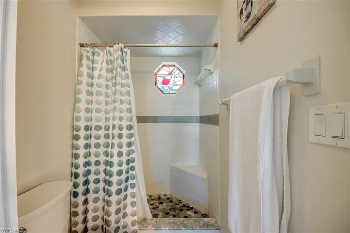 Shower with mosaic pebble flooring, built-in bench, and a decorative stained-glass window