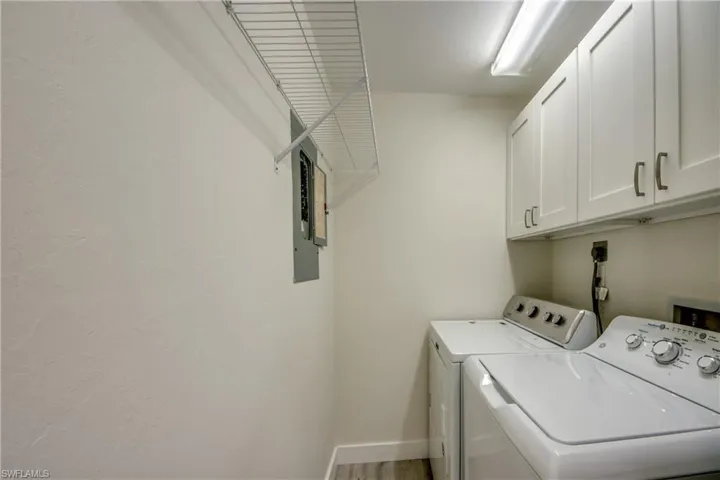 Dedicated laundry area featuring white shaker-style cabinetry with brushed nickel hardware, a wire storage shelf, overhead fluorescent lighting, and wood-finish flooring