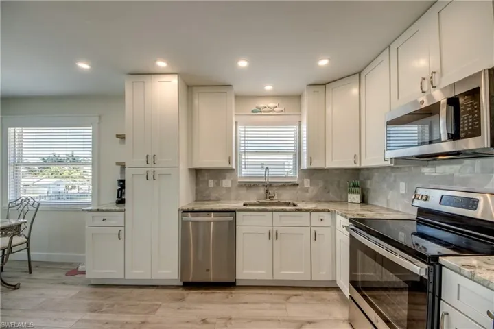 Modern kitchen featuring white shaker cabinetry, granite countertops, stainless steel appliances, a tiled backsplash, and wood-finish flooring