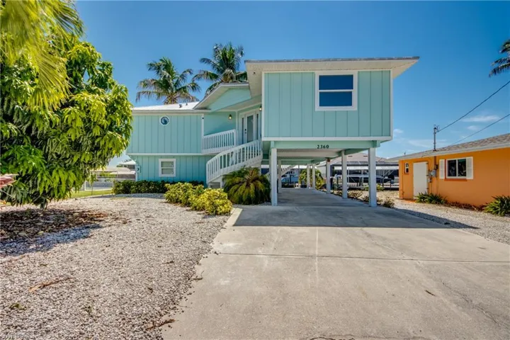 Stilted coastal residence featuring light blue siding, a white spiral staircase, and a concrete driveway