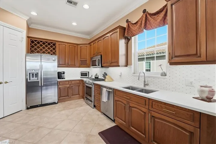 Kitchen with appliances with stainless steel finishes, brown cabinets, ornamental molding, recessed lighting, and tasteful backsplash
