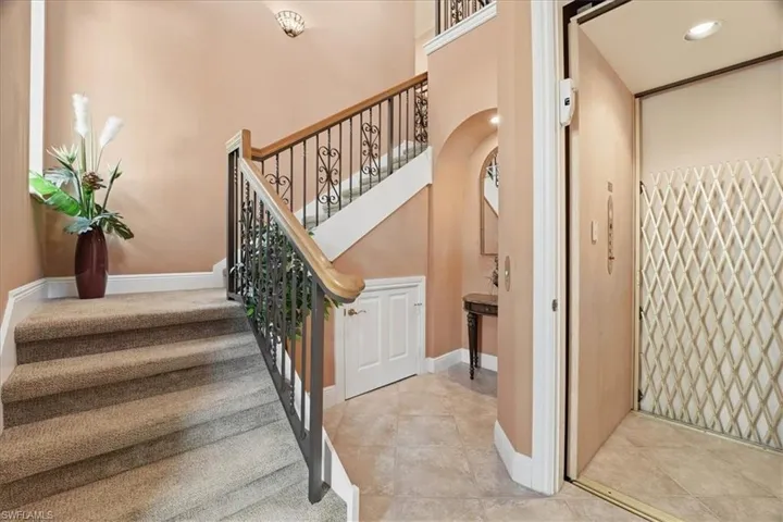 Stairs with elevator, arched walkways, tile patterned floors, and recessed lighting