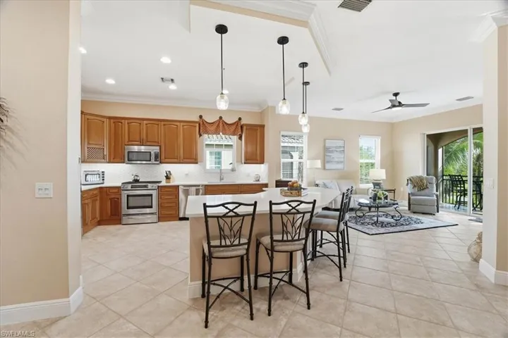 Kitchen with decorative light fixtures, a kitchen bar, ornamental molding, appliances with stainless steel finishes, and open floor plan
