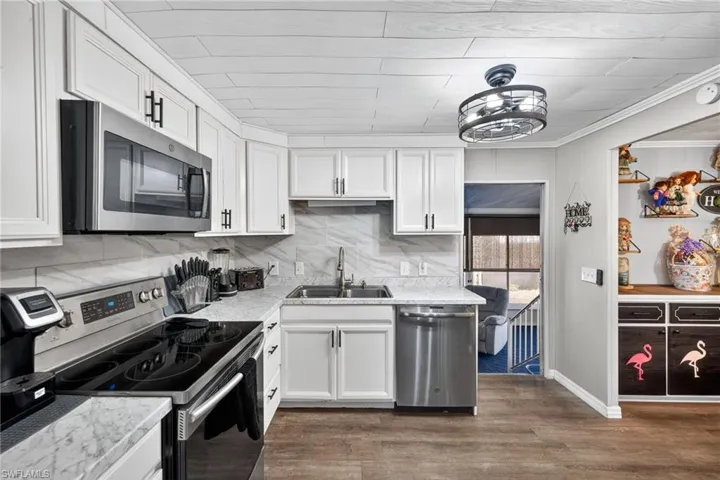 Kitchen with stainless steel appliances, light countertops, white cabinets, dark wood-style floors, and ornamental molding