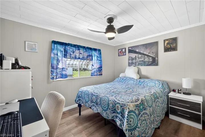 Bedroom with wood finished floors, an office area, ceiling fan, and wood walls