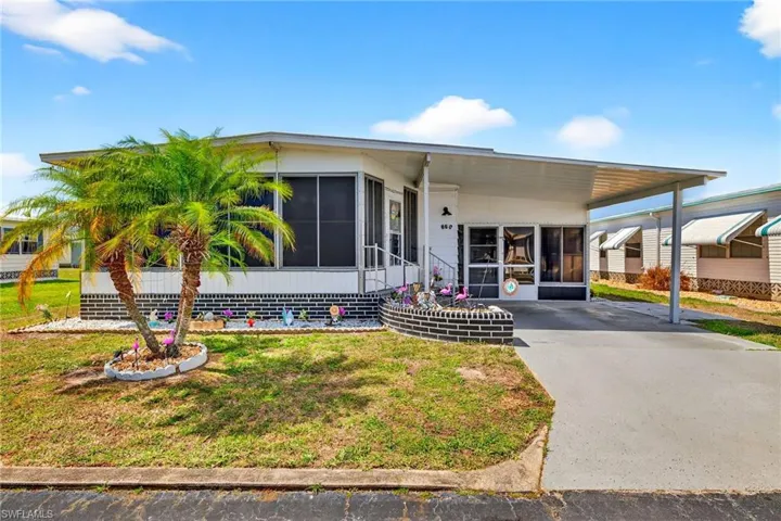 Manufactured / mobile home featuring a sunroom, an attached carport, a front lawn, and driveway