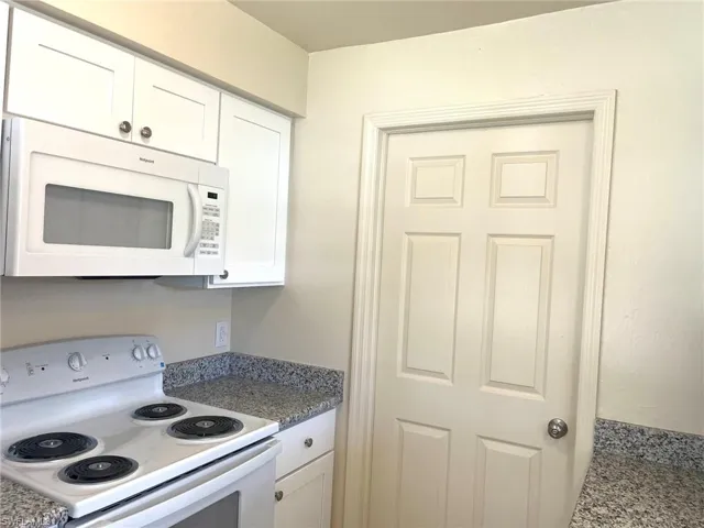 Kitchen with white appliances, white cabinetry, and dark stone counters