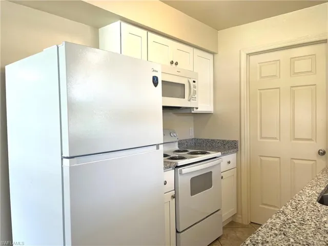 Kitchen with white appliances, white cabinets, light tile patterned floors, and dark stone countertops