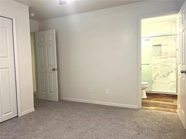 Unfurnished bedroom with dark carpet, ensuite bathroom, and a ceiling fan