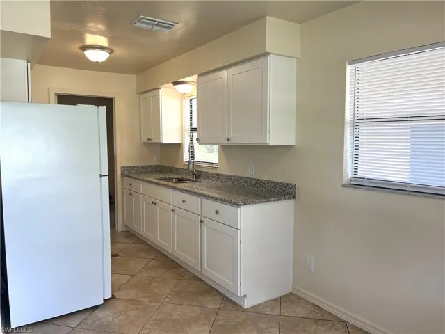 Kitchen with freestanding refrigerator, dark stone counters, white cabinets, and light tile patterned floors
