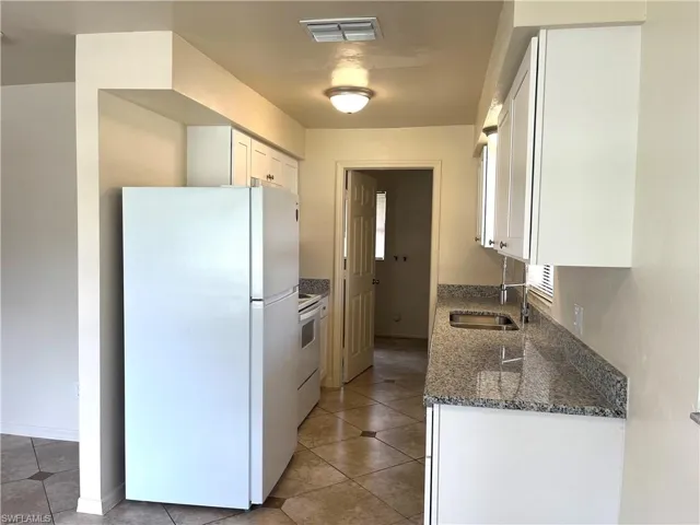 Kitchen with white appliances, dark stone counters, white cabinetry, and light tile patterned floors
