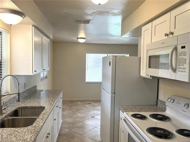 Kitchen with white cabinets, white appliances, dark stone countertops, and light tile patterned floors