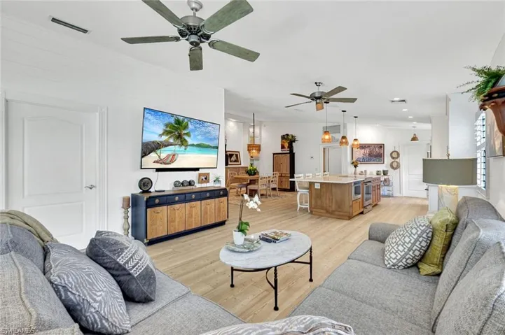 Light wood-finish flooring throughout, two ceiling fans with lighting, recessed lighting, and a kitchen island with seating
