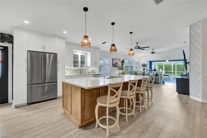 Kitchen featuring white shaker cabinetry, stainless steel refrigerator, large center island with seating, and wood-finish flooring