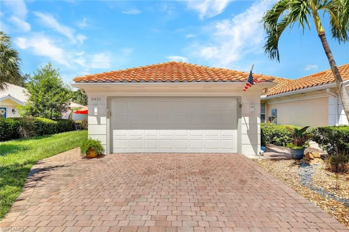 Brick paver driveway, attached garage, tile roof, and landscaped grounds