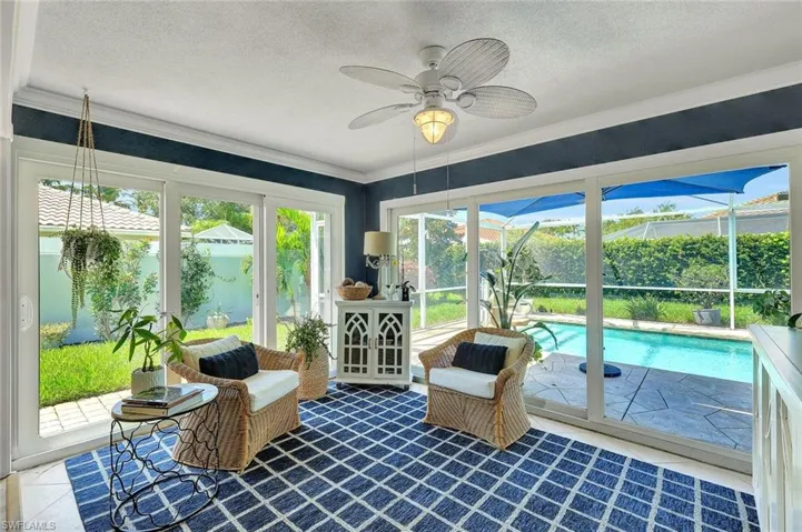 Expansive sliding glass doors, ceiling fan, crown molding, and direct access to a paved patio and swimming pool