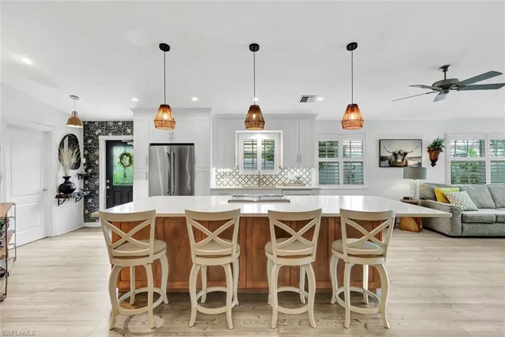 Expansive kitchen island with seating, white shaker cabinetry, stainless steel French door refrigerator, patterned tile backsplash, and light wood-finish flooring