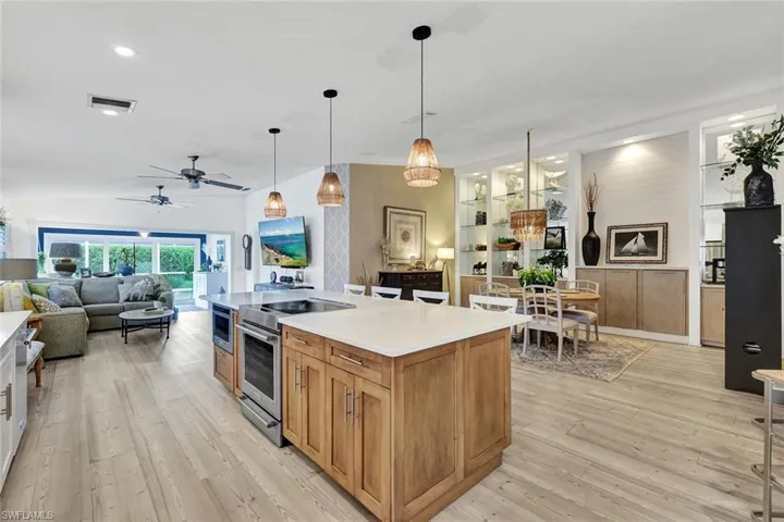 Spacious open-concept interior with wood-finish flooring, a kitchen island featuring integrated stainless steel appliances, and built-in shelving with recessed lighting
