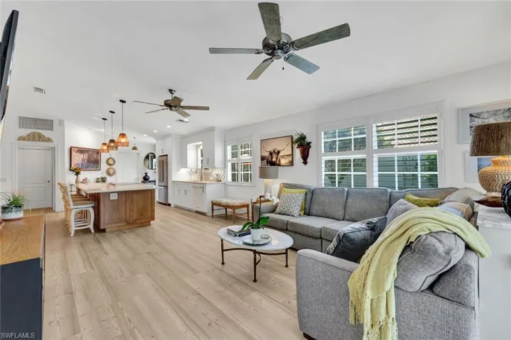 Open-concept living space featuring wood-finish flooring, multiple windows, built-in cabinetry, and ceiling fans