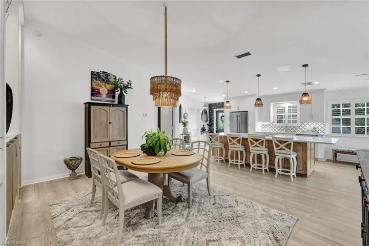 Open-concept layout featuring wood-finish flooring, a kitchen island with seating, pendant lighting, and white cabinetry