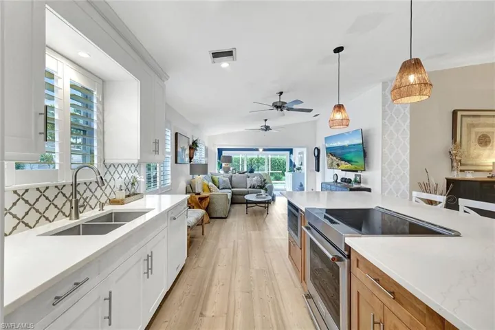 Open-concept kitchen with white shaker cabinetry, patterned tile backsplash, stainless steel double basin sink, and a center island with integrated cooktop