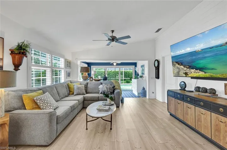 Vaulted ceiling with a ceiling fan, light wood-finish flooring, white plantation shutters, and shiplap accent wall