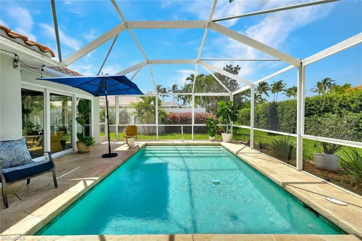 Screen-enclosed pool featuring a rectangular design, adjacent patio with stone-finish pavers, and lush perimeter landscaping
