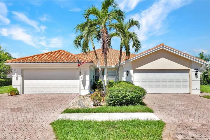 Tiled roofing, stucco exterior, dual garage doors, paved driveway, and mature palm trees