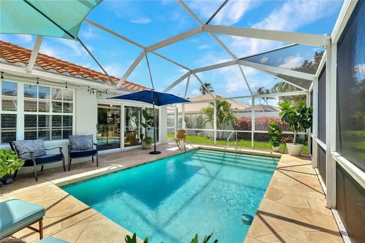 Screened-in swimming pool with a stone paver deck, white exterior walls, and a terracotta tile roof