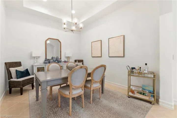Dining room with light tile patterned floors, baseboards, a tray ceiling, and an inviting chandelier